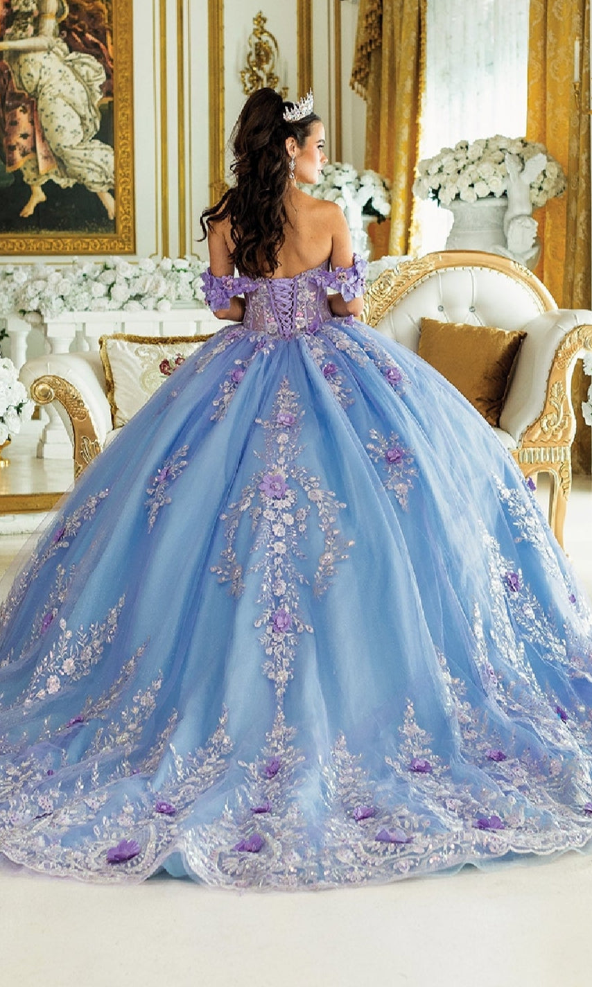 A woman in the Blue Quinceanera Dress 1999 By Dancing Queen, featuring a tiara and purple floral embellishments, stands in an elegant gold-decorated room.